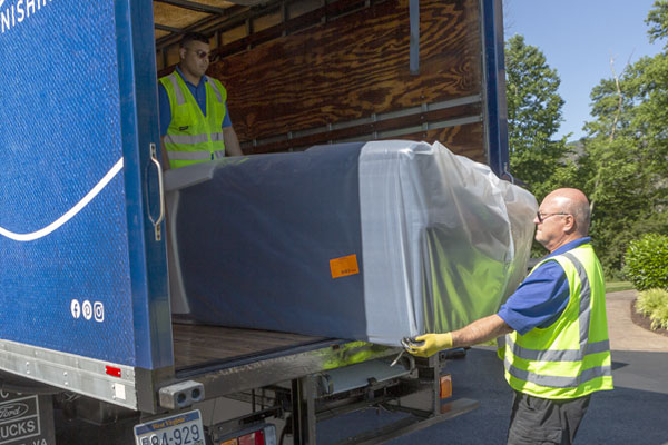 two delivery people pulling a sofa off a truck